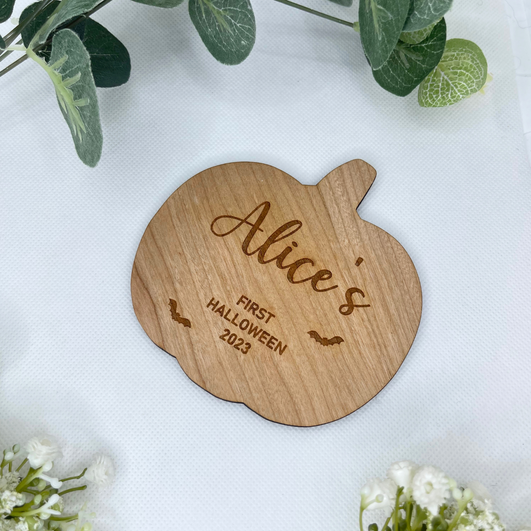 A 15x15cm custom pumpkin-shaped baby's first Halloween plaque, meticulously carved from cherry wood. The plaque features the adorable engraving of bats and can be personalised with your baby's first name. This 4mm thick keepsake beautifully captures the essence of your little one's inaugural Halloween, preserving the memory for years to come.
