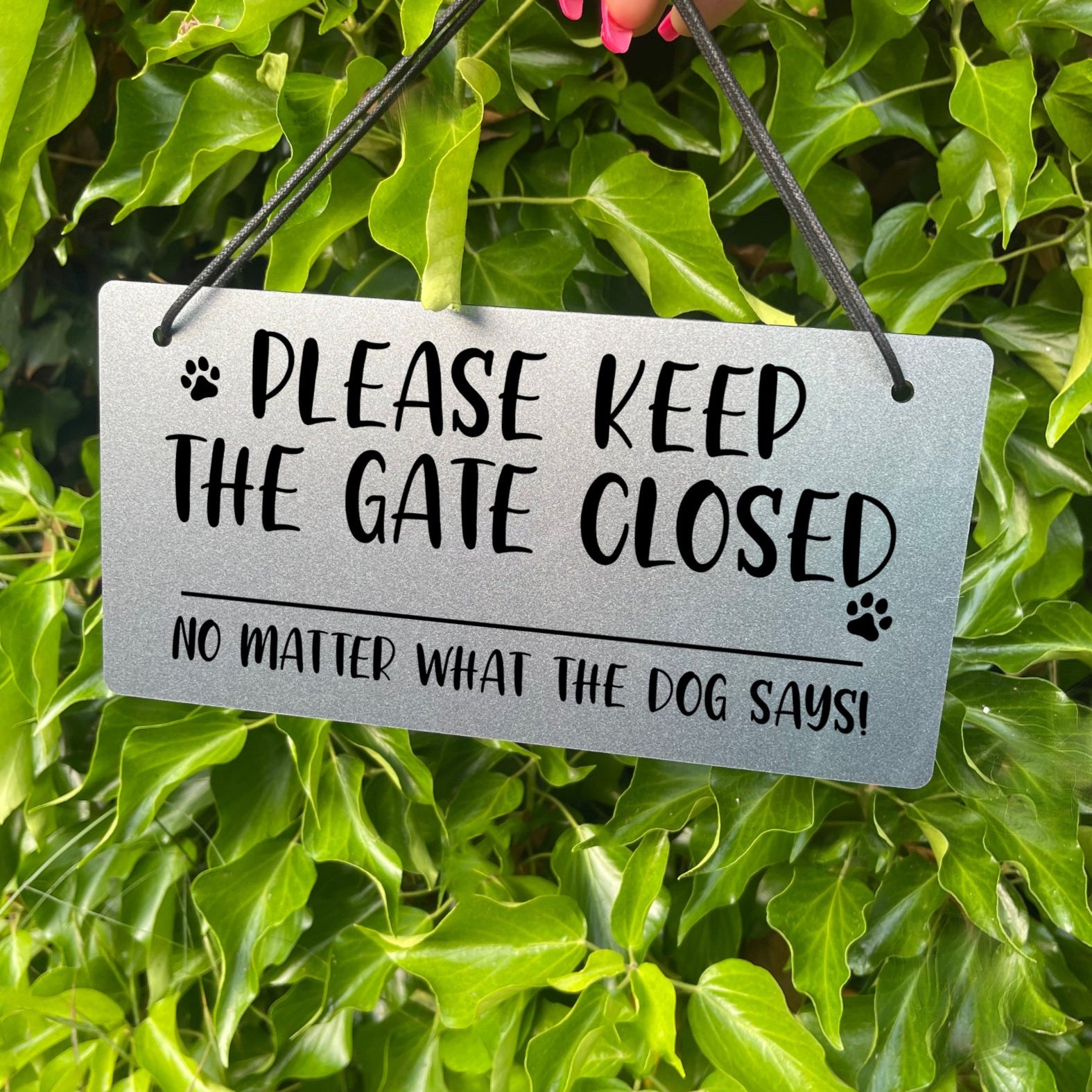 "Silver Laser-Engraved 'Please Keep the Gate Closed' Sign with Paw Print Illustration" Description: Close-up of a silver-colored acrylic sign with laser-engraved text that reads "Please Keep the Gate Closed, No Matter What the Dog Says." The sign features a cute paw print illustration, adding a playful touch.