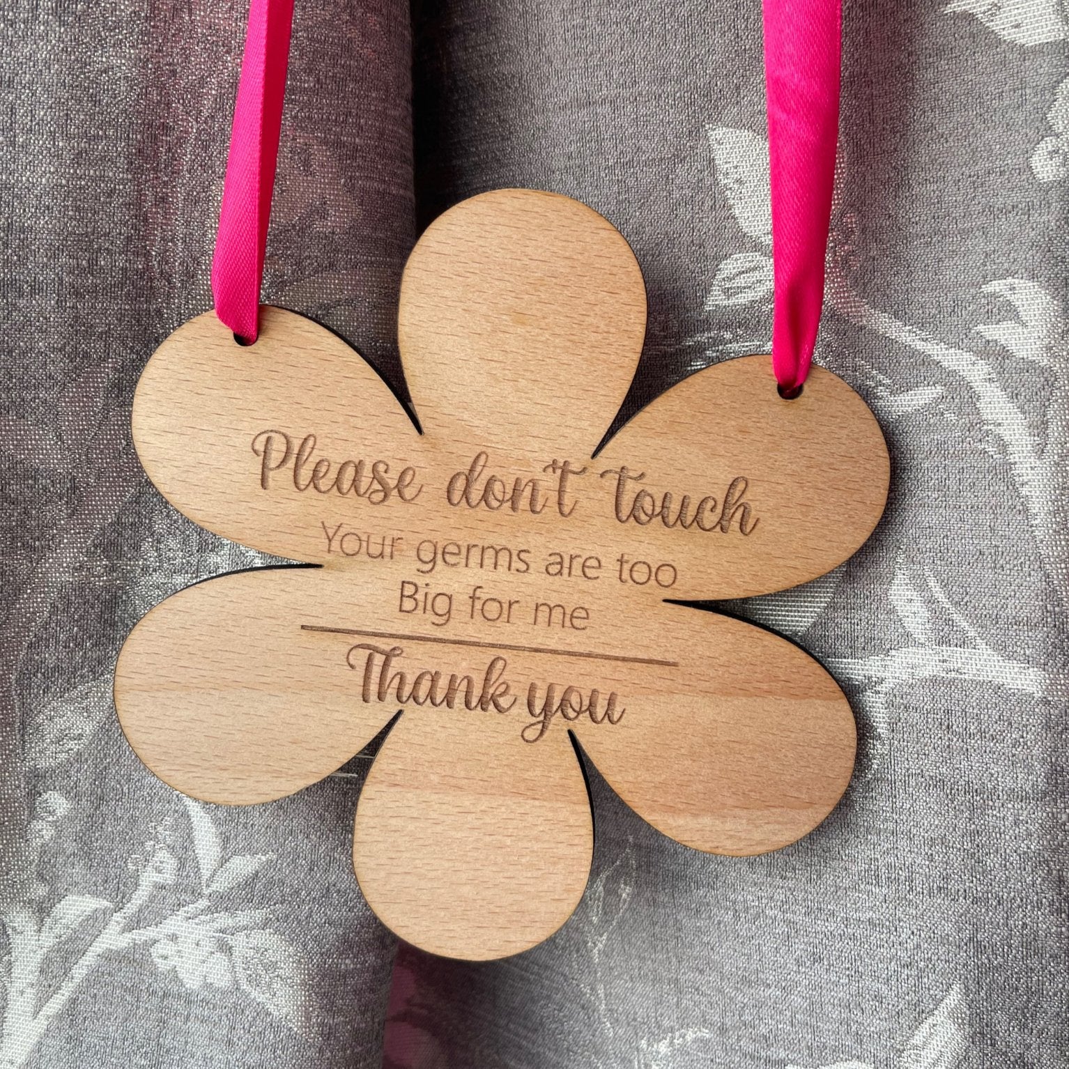 Embrace the beauty of motherhood with our protective flower-shaped beech wood hanging sign. Measuring 145mm by 148mm and crafted from durable 4mm wood, this enchanting piece serves as both a stylish decoration and a shield for your precious one. Engraved with 'Please do not touch, your germs are too big for me, thank you,' and available with your choice of blue or pink ribbon.