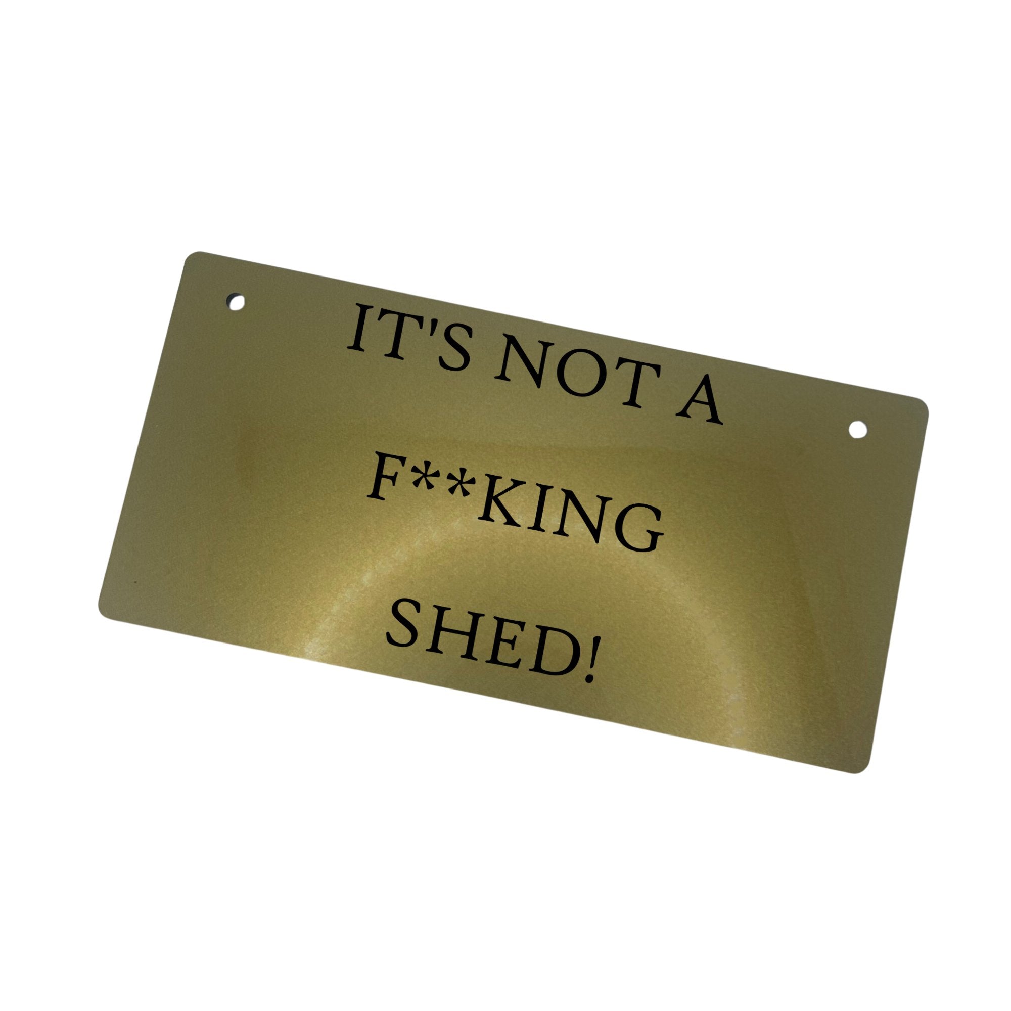 Alt Text: "Gold 'IT'S NOT A FKING SHED' Sign: Distinctive and Eye-Catching" Description: An angled view of the gold-colored acrylic sign displaying the engraved text "IT'S NOT A FKING SHED." The sign's design adds a distinctive touch to any space.