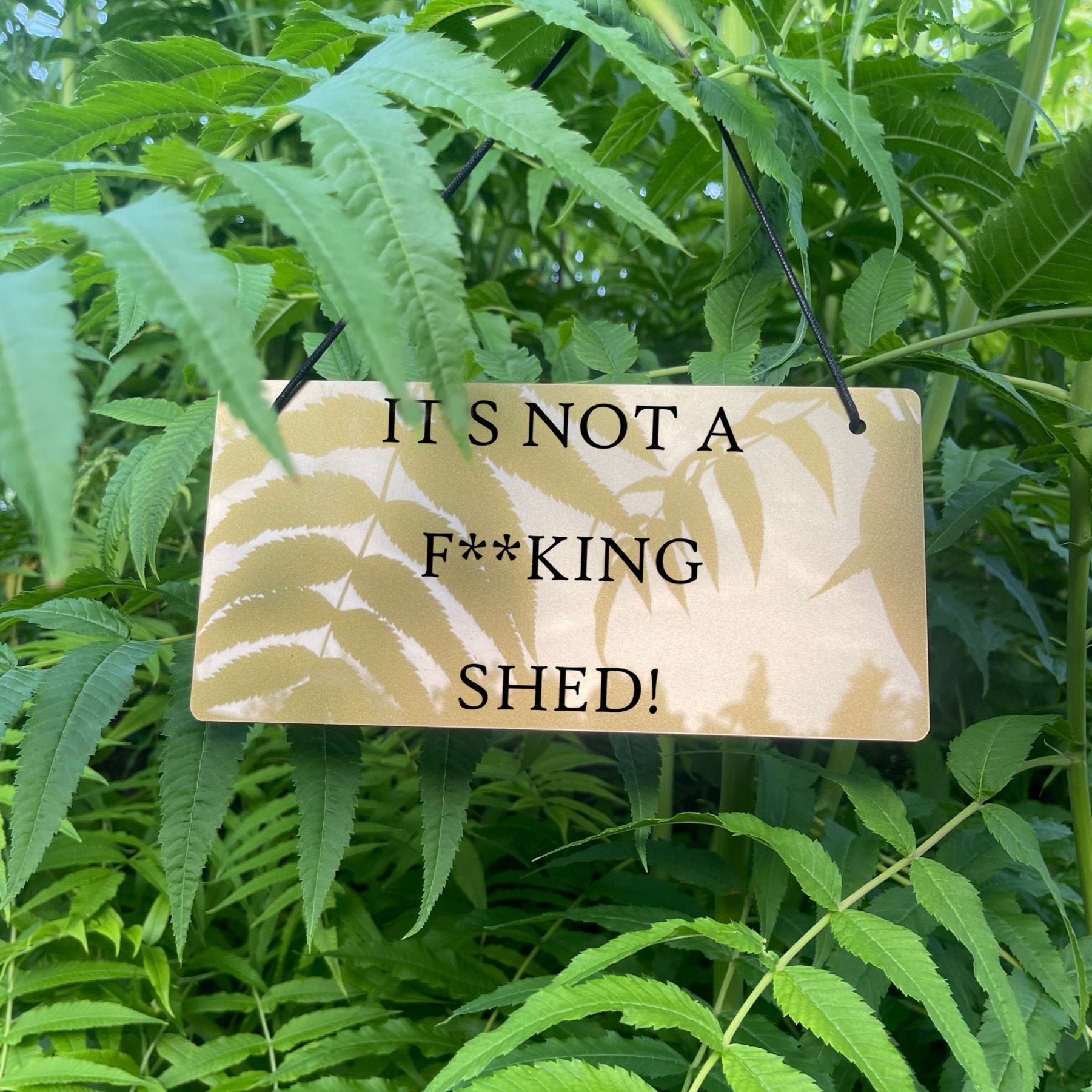 "Durable and Waterproof 'IT'S NOT A F**KING SHED' Sign" Description: A view of the sign in an outdoor setting, showcasing its durability and waterproof features. The engraved message remains intact even in various weather conditions.