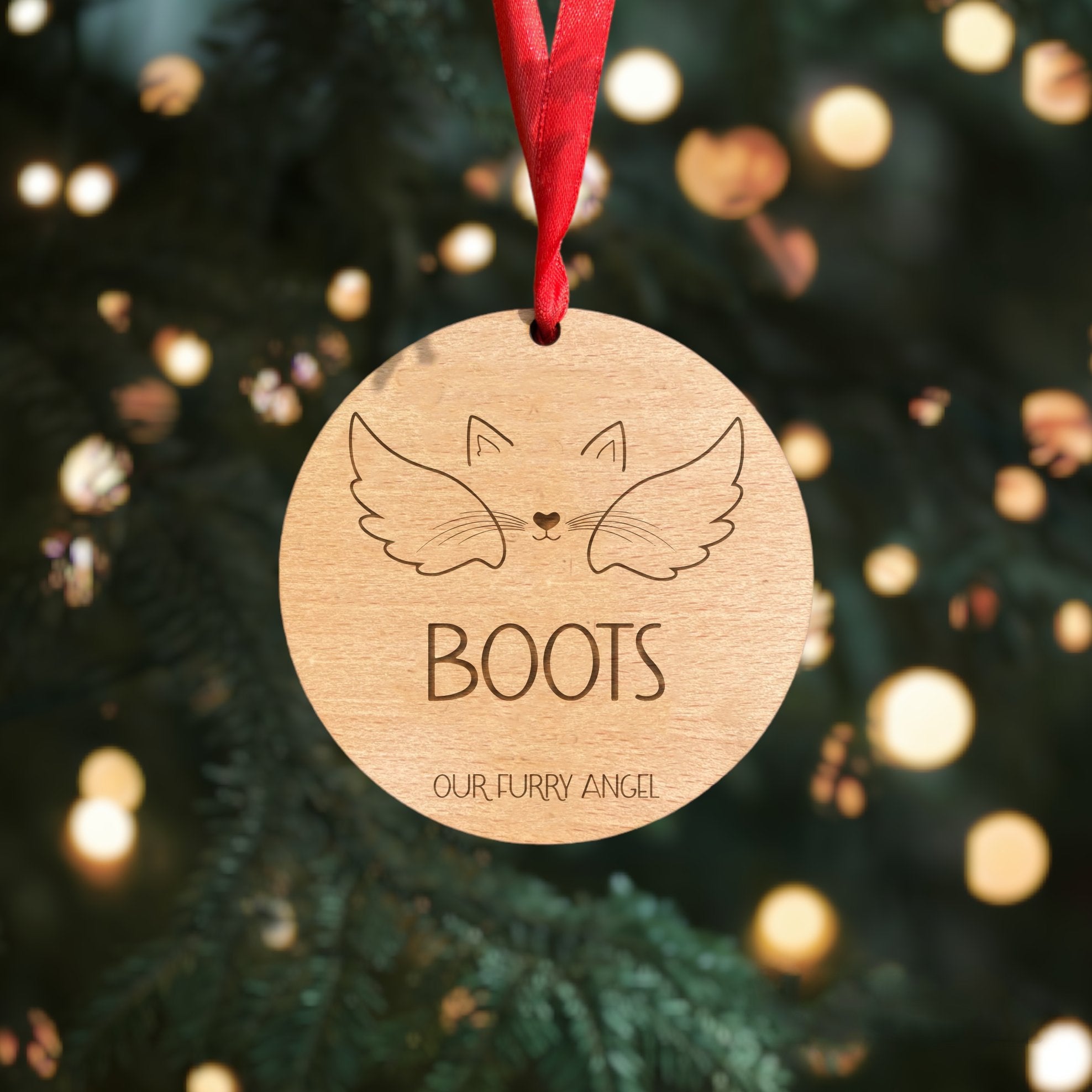 Personalised wooden memorial cat bauble with name, ears, nose, mouth, and whiskers details. Crafted from 4mm beech veneer wood with a classic red ribbon. A special tribute to your furry angel for the holidays. Writing at the bottom reads 'Our furry angel.