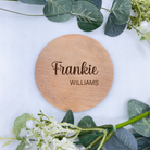 Round personalised baby announcement plaque in beech veneer, elegantly engraved with the baby's name, shown against a nursery backdrop for context.