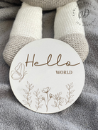 Elegant white MDF 'Hello World' baby plaque featuring a flower design and engraved text, a sweet addition to baby announcement photos.