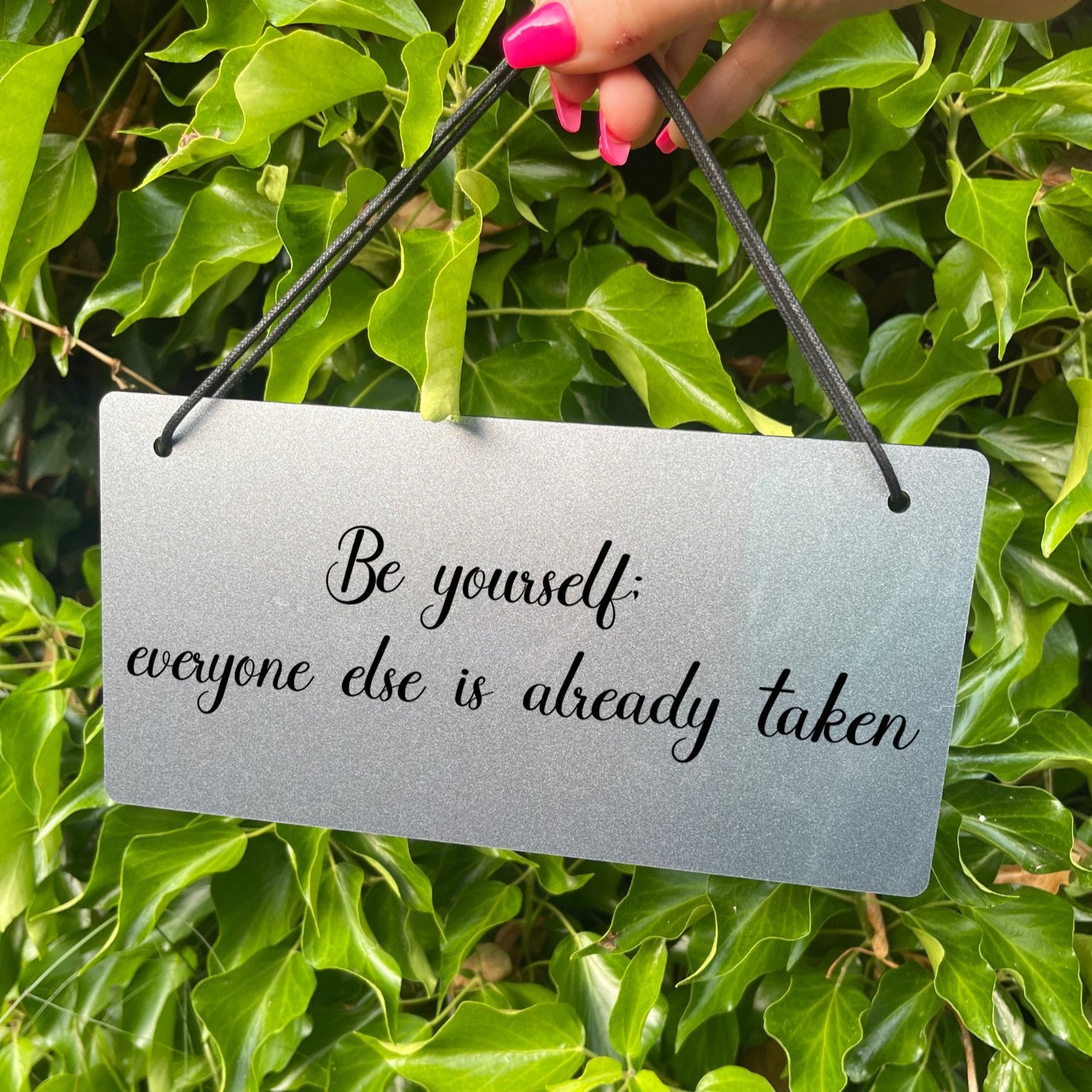Acrylic sign with the quote 'Be yourself; everyone else is already taken,' hung with black twine. Ideal for home decor and as a meaningful gift for special occasions.