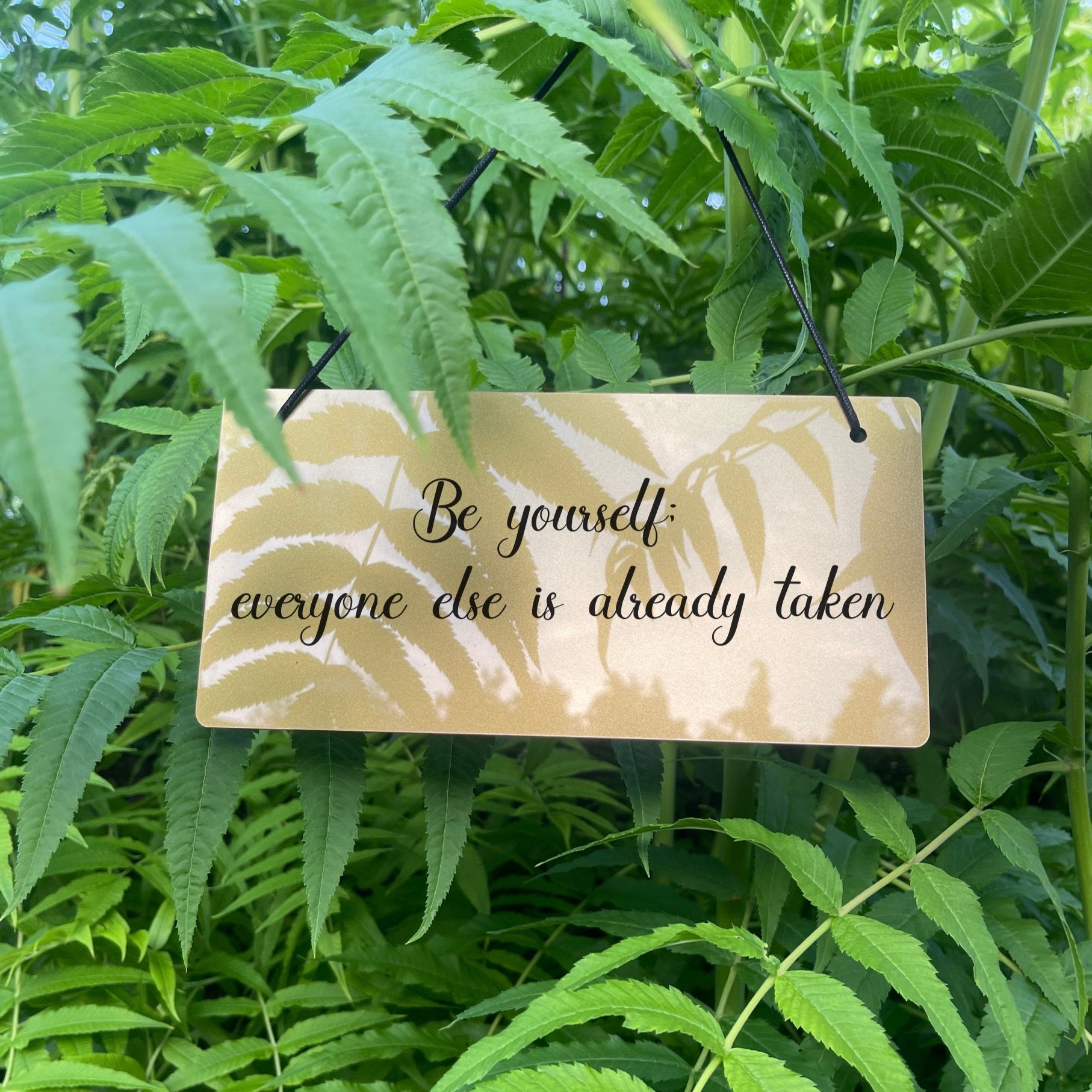 Premium silver or gold acrylic sign with black twine hanging, featuring the quote 'Be yourself; everyone else is already taken.' A stylish addition to home decor and a thoughtful gift option for special occasions.