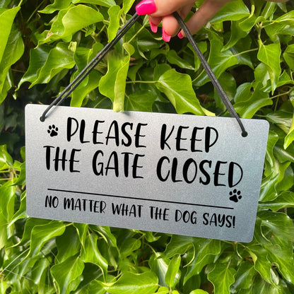 "Silver Laser-Engraved 'Please Keep the Gate Closed' Sign with Paw Print Illustration" Description: Close-up of a silver-colored acrylic sign with laser-engraved text that reads "Please Keep the Gate Closed, No Matter What the Dog Says." The sign features a cute paw print illustration, adding a playful touch.