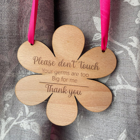 Embrace the beauty of motherhood with our protective flower-shaped beech wood hanging sign. Measuring 145mm by 148mm and crafted from durable 4mm wood, this enchanting piece serves as both a stylish decoration and a shield for your precious one. Engraved with 'Please do not touch, your germs are too big for me, thank you,' and available with your choice of blue or pink ribbon.
