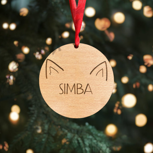 A customized wooden pet bauble for Christmas made of 4mm beech veneer wood. The ornament features a pet's name and cute ears, with a red ribbon for a classic, festive look. Perfect for celebrating the holidays with your furry friend. 🎄🐾
