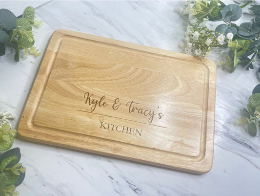 Personalised Engraved Wooden Chopping Board, personalise your chopping board with a name on the left and side and name on the right,  underneath is a line then at the bottom the word kitchen with a little chefs hat above the K. This is make from  Hevea Wood & the size is 300mmX200mm. Perfect gift for any couple. 