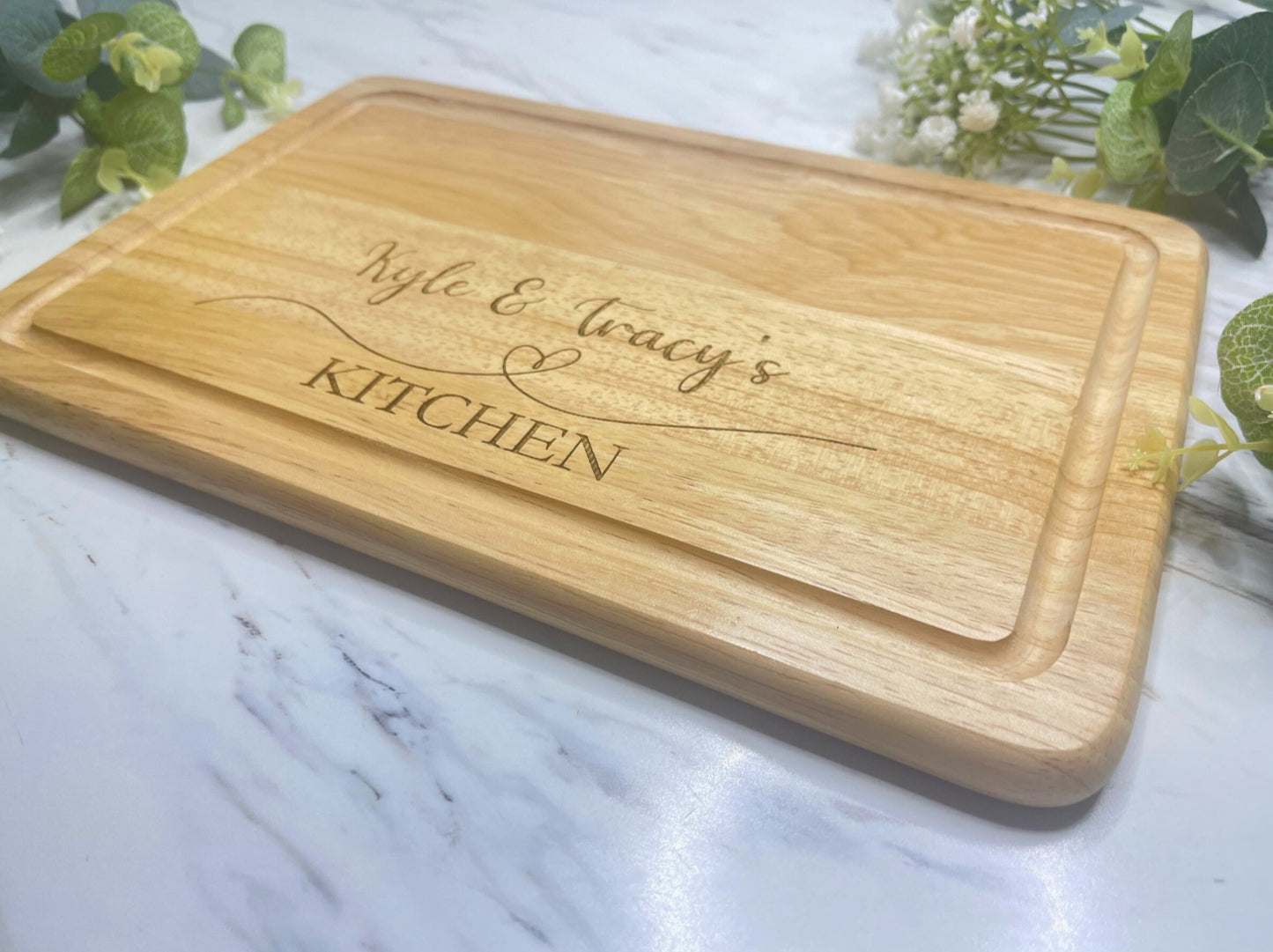 Personalised Engraved Wooden Chopping Board, personalise you5r chopping board with a name on the left and side and name on the right, underneath is a heart then the word kitchen at the bottom. This is make from Hevea Wood & the size is 300mmX200mm. Perfect gift for any couple.