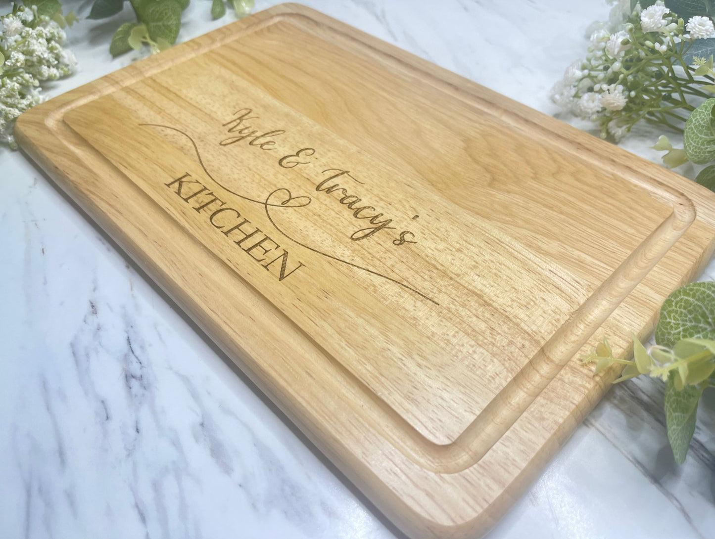 Personalised Engraved Wooden Chopping Board, personalise you5r chopping board with a name on the left and side and name on the right, underneath is a heart then the word kitchen at the bottom. This is make from Hevea Wood & the size is 300mmX200mm. Perfect gift for any couple.